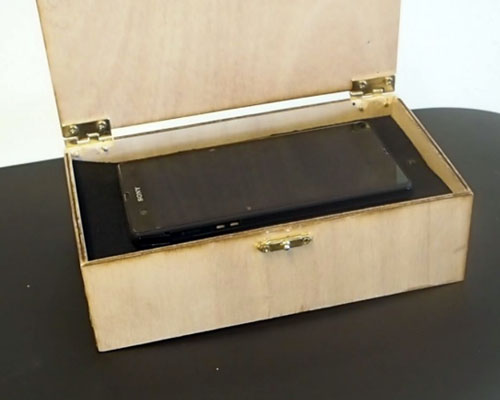 A wooden box with a mobile phone placed inside and lid open