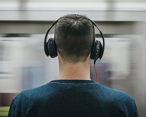 A man from the behind, sitting with headset on the subway.