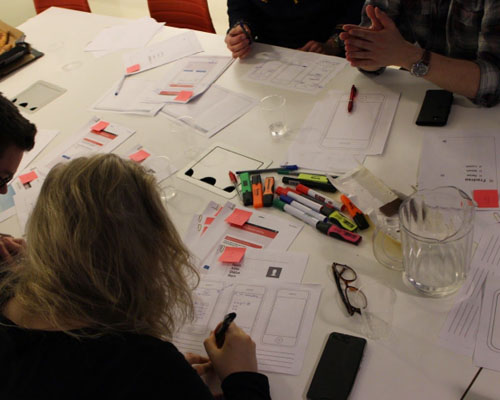 People working in a workshop, with papers and posts scattered around the table
